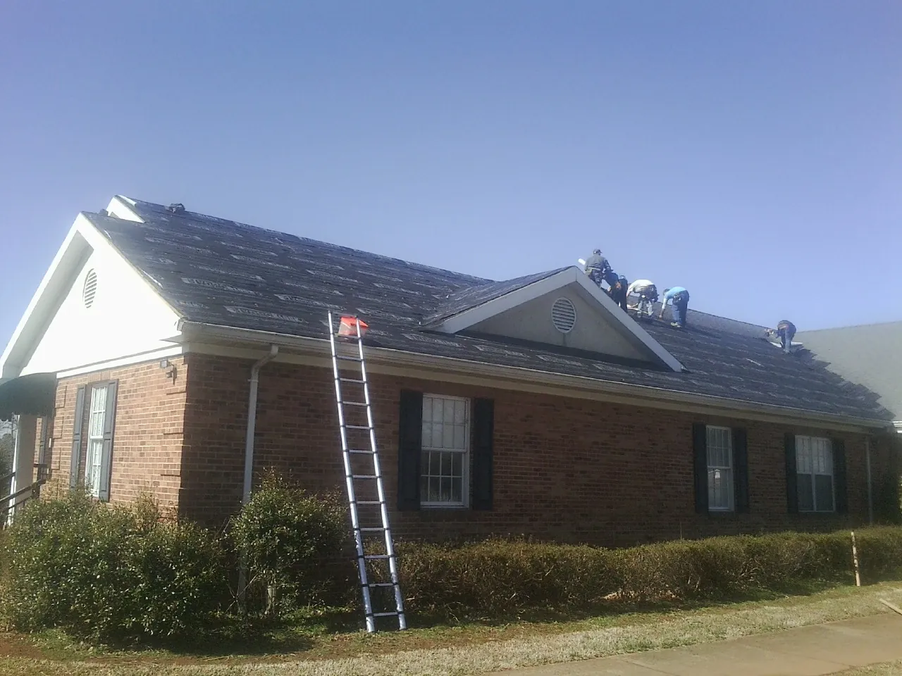 Crew tearing shingles off a brick ranch roof with a ladder set — Emergency Roof Repair work by our crew in Wood Lake
